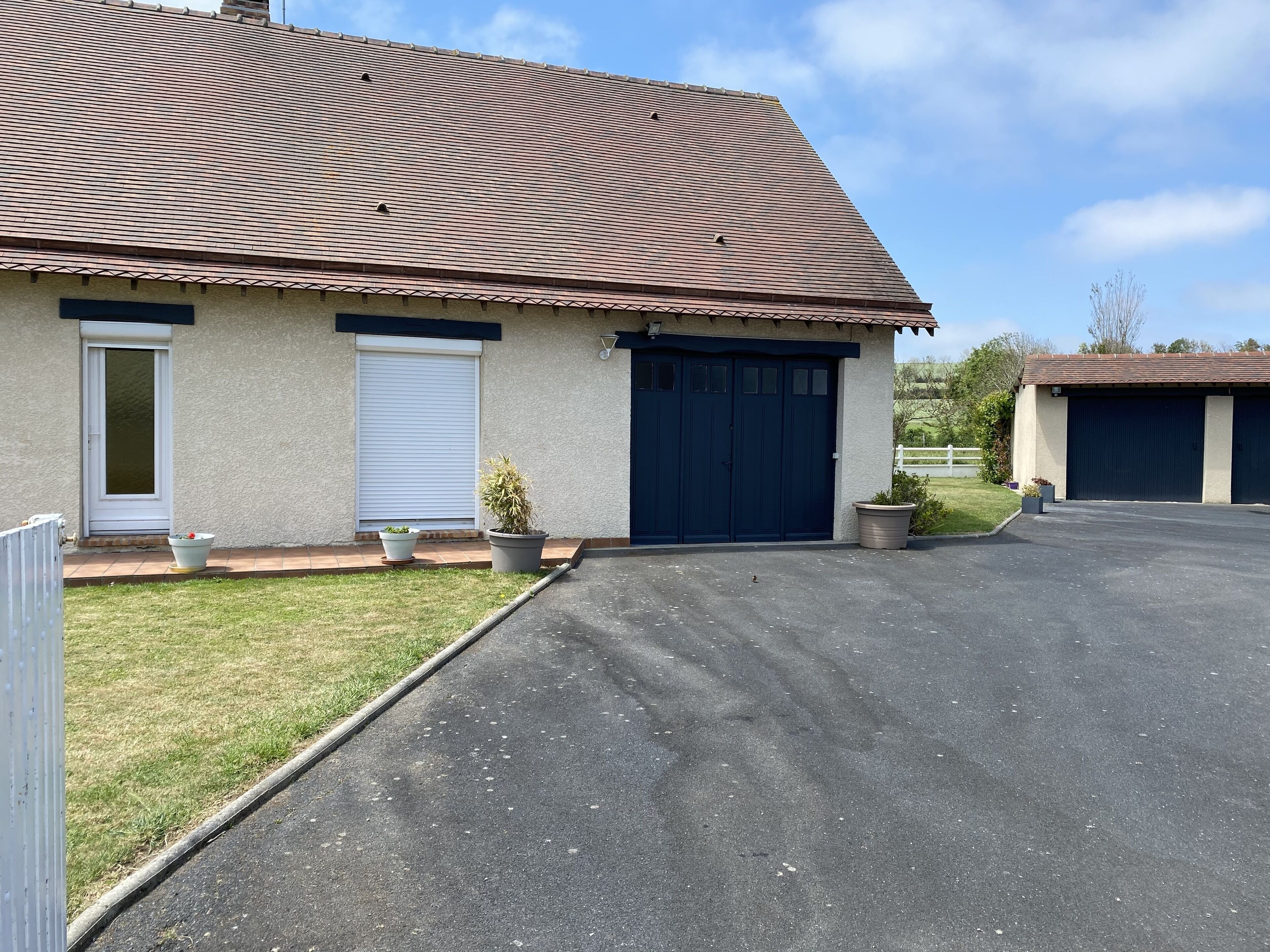 Un bâtiment à deux étages, doté d’un toit recouvert de tuiles, d’un garage et d’une allée pavée.