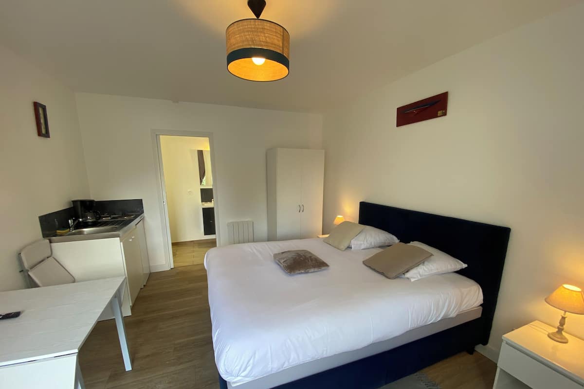 Hotelkamer met een bed, nachtkastjes, een bureau, een kitchenette en een badkamer zichtbaar door een open deur.
