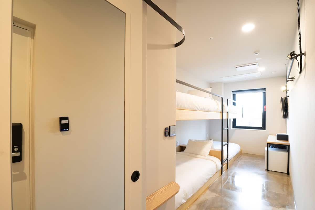 A modern hotel room with bunk beds, a desk, and a bathroom.