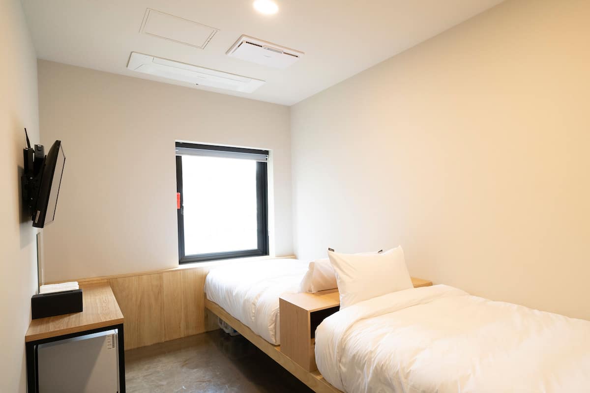 A modern, minimalist bedroom with two single beds, a small desk, and a built-in wardrobe.