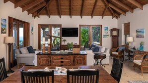 A spacious living area with a wooden dining table, sofas, and a TV mounted on the wall.