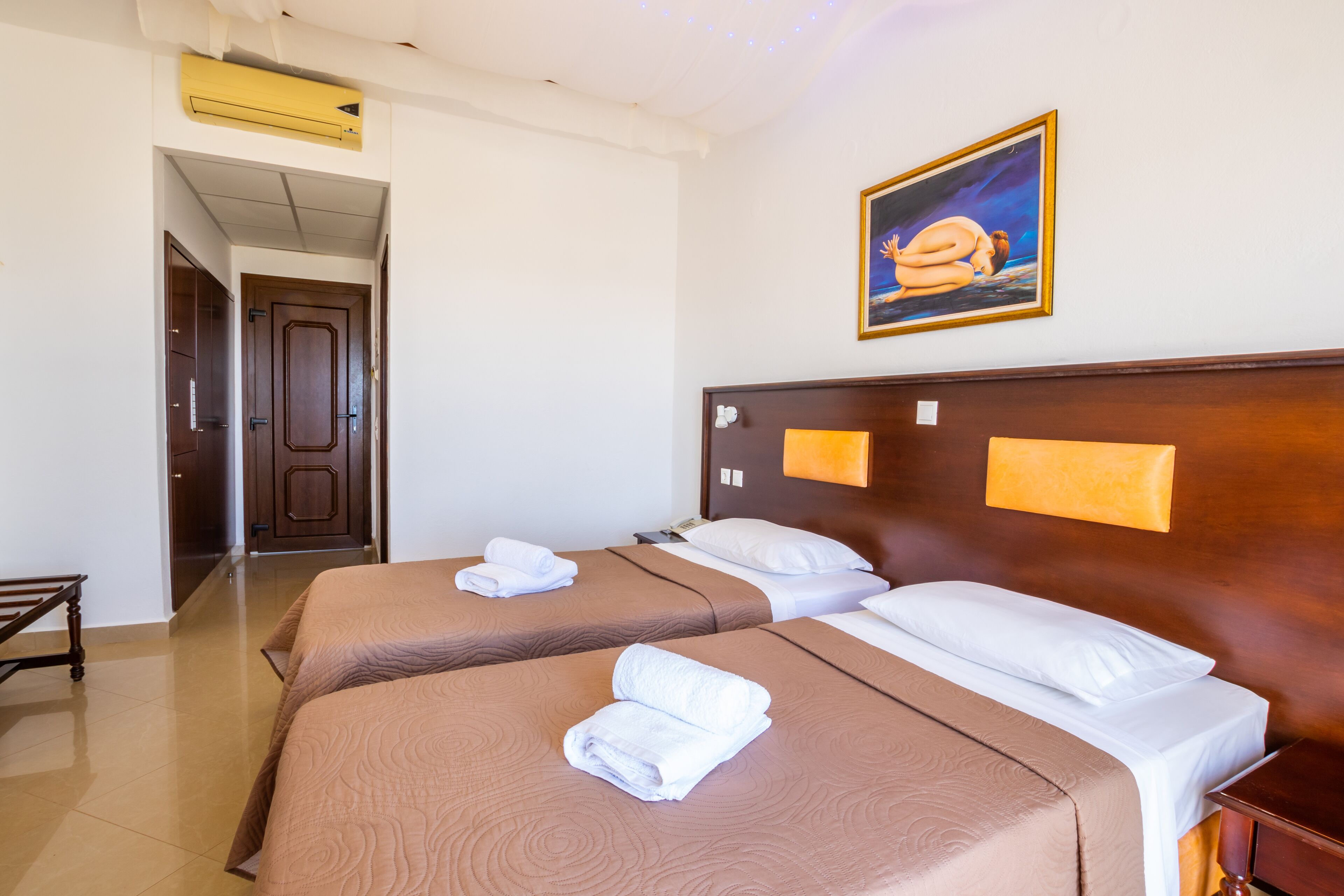 Una habitación de hotel con dos camas, un cuadro en la pared y una puerta que da a otra habitación.