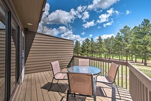 A wooden deck with a glass table and two chairs, overlooking a grassy area with trees. - Fireplace & Mtn Views: Estes Park Home w/ Deck! (Estes Park)