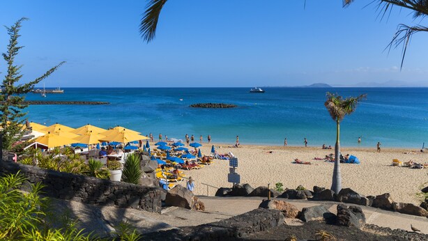 Ein Strand mit Sonnenschirmen, Menschen und einem Boot im Wasser.