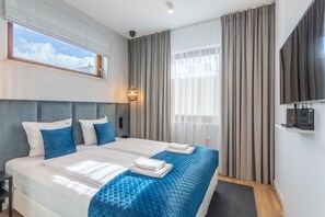 A hotel room with two beds, a large window, a flat-screen TV, and a wall-mounted TV.