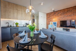 A modern kitchen with wooden cabinets, a dining table set with napkins, and a TV mounted on a brick wall. - Ferienwohnung am Meer, Urlaub auf der Insel Usedom, Appartement Anker (Świnoujście)