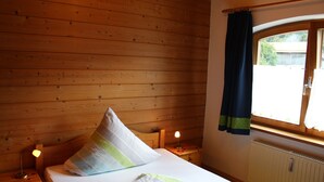 Um quarto com painéis de madeira, uma cama, uma mesinha de cabeceira, um abajur e uma janela com cortinas.