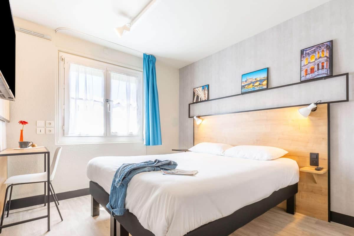 Una habitación de hotel moderna con cama, mesita de noche, escritorio, silla y una obra de arte en la pared.