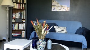 Una sala de estar con un sofá azul, una mesa de centro blanca, una estantería y una lámpara.
