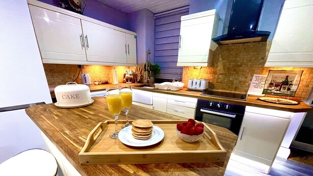 A modern kitchen with white cabinets, a wooden countertop, a toaster, and a tray with pancakes and orange juice. - Sleeps 8 Snowdonia North Wales Nr Zip World (Blaenau Ffestiniog)