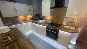 A modern kitchen with white cabinetry, a black stove, and a wooden countertop. - Sleeps 8 Snowdonia North Wales Nr Zip World (Blaenau Ffestiniog)