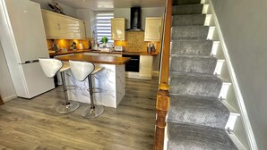 A kitchen with a central island, bar stools, and a staircase. - Sleeps 8 Snowdonia North Wales Nr Zip World (Blaenau Ffestiniog)