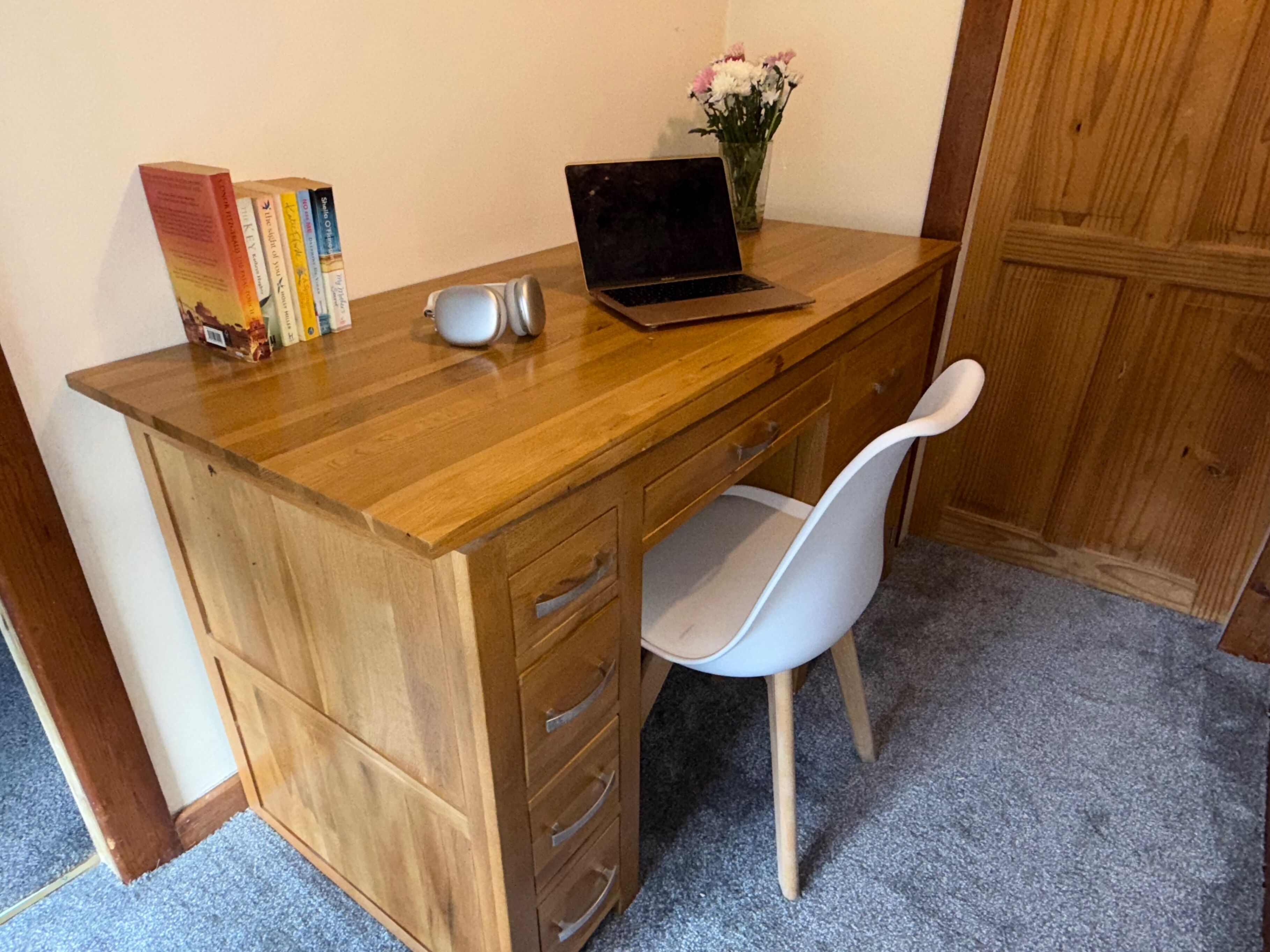 Un escritorio de madera con una computadora portátil, libros y un florero con flores.