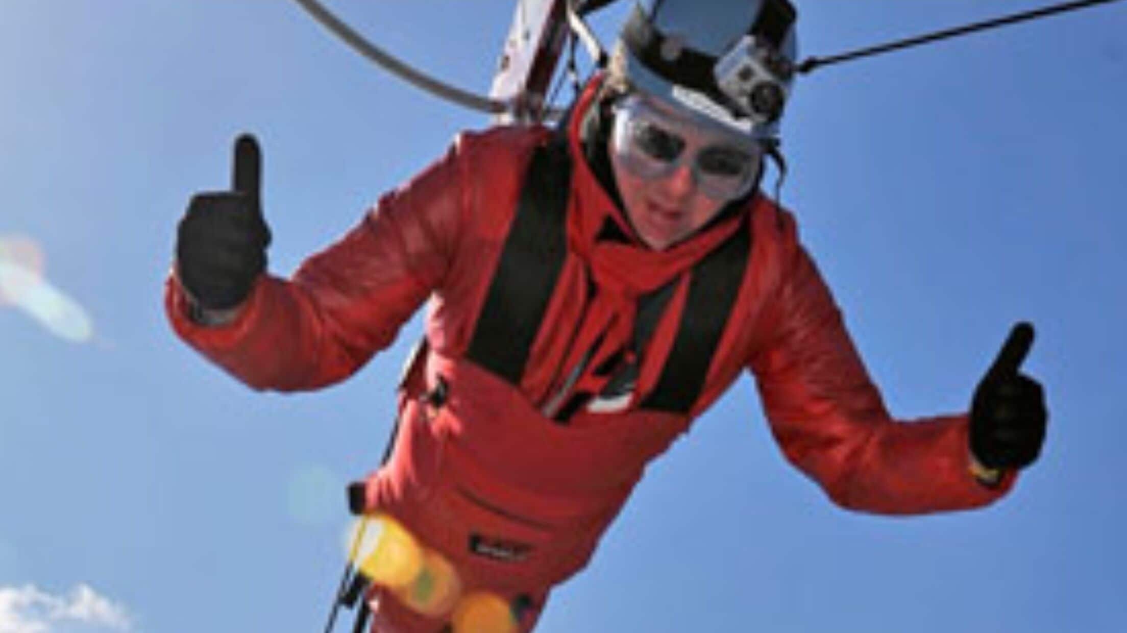 Persoon in een rode jas en helm, die duimpje omhoog steekt.