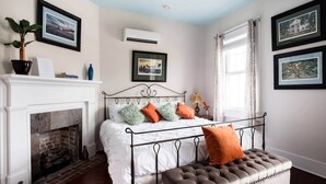 A bedroom with a fireplace, a bed with a metal frame, and framed pictures on the wall. - Charming Suite in the Heart of Charleston (Charleston)