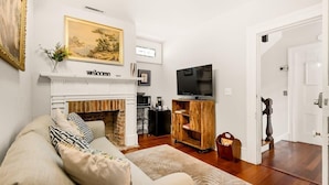A living room with a fireplace, a sofa, a television, and a wooden cabinet. - The Gallery Suite - by MUSC ★FREE PARKING★ (Charleston)