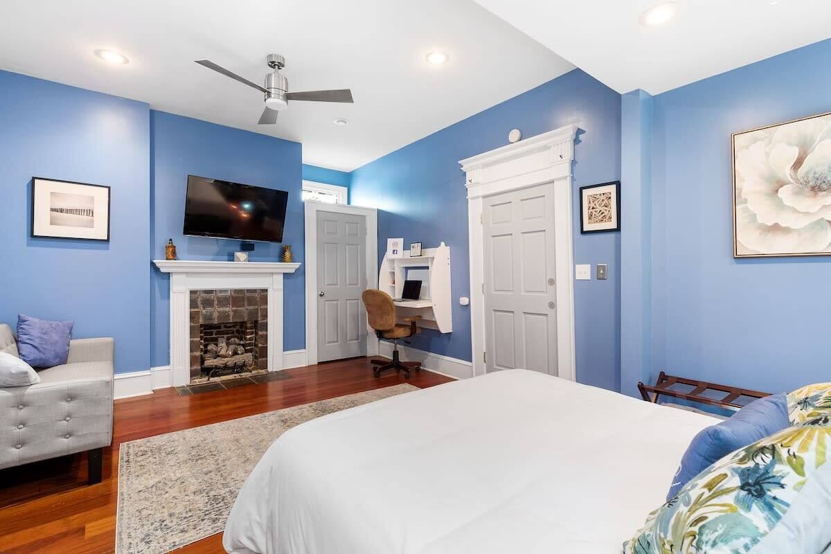A bedroom with blue walls, a fireplace, a bed, a desk, and a TV.
