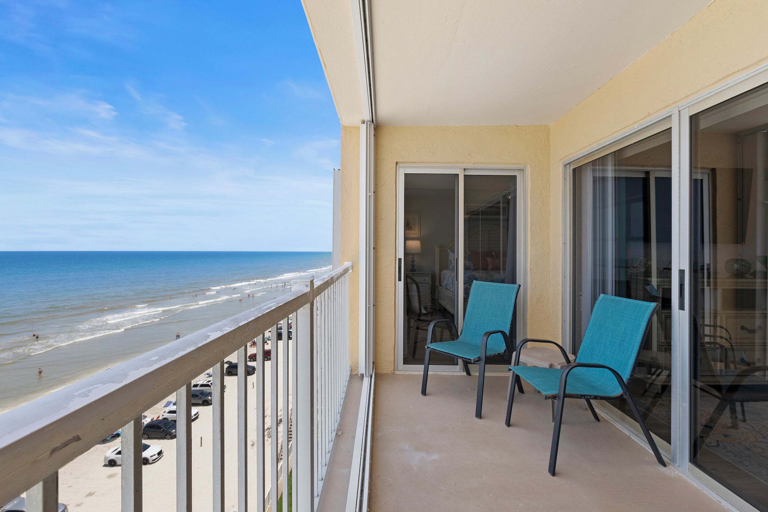 A balcony with a view of the beach, two chairs, and a sliding glass door.