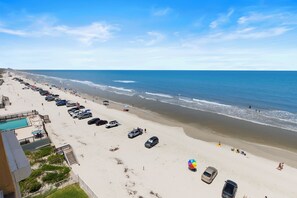 Une plage avec une piscine, des voitures garées et des parasols.