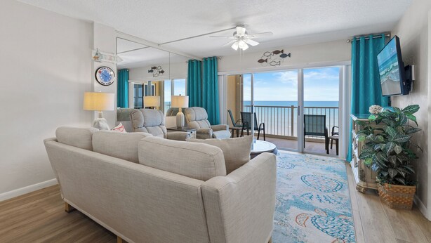 A living room with a sofa, chairs, a TV, and a balcony with a view. - Stunning Oceanfront Condo with Spectacular Views of NSB (New Smyrna Beach)