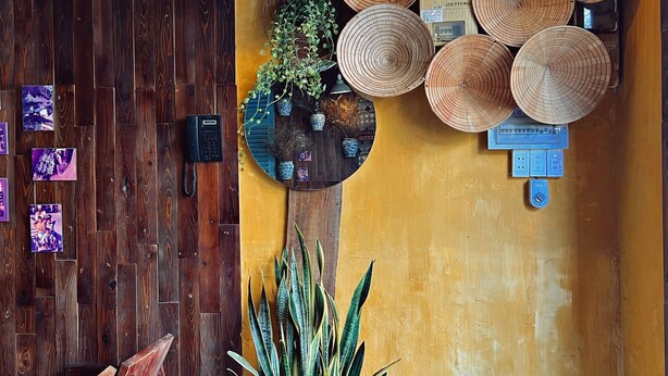 A wooden interior with a yellow wall, a ceiling fan, a hanging light fixture, and a wall-mounted power outlet. - Nha Saigon (Ho Chi Minh City)