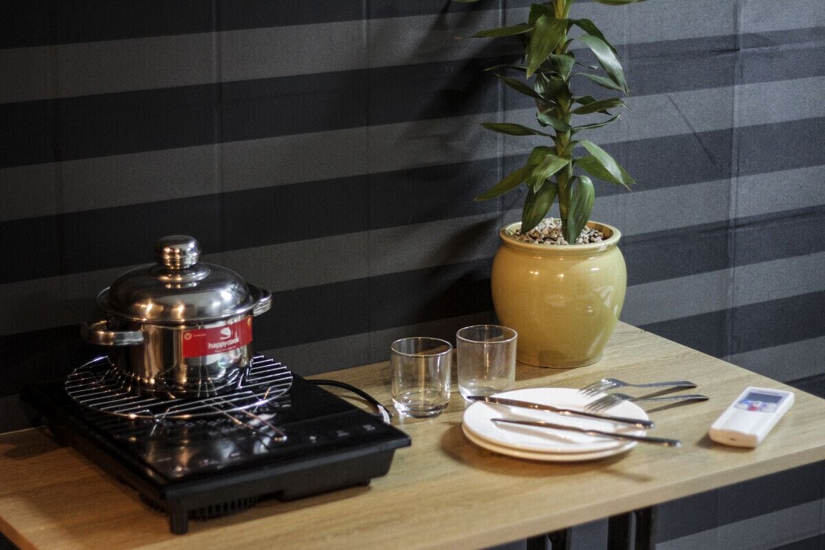 A table with a portable stove, a pot, two glasses, a plate with cutlery, and a mobile phone.