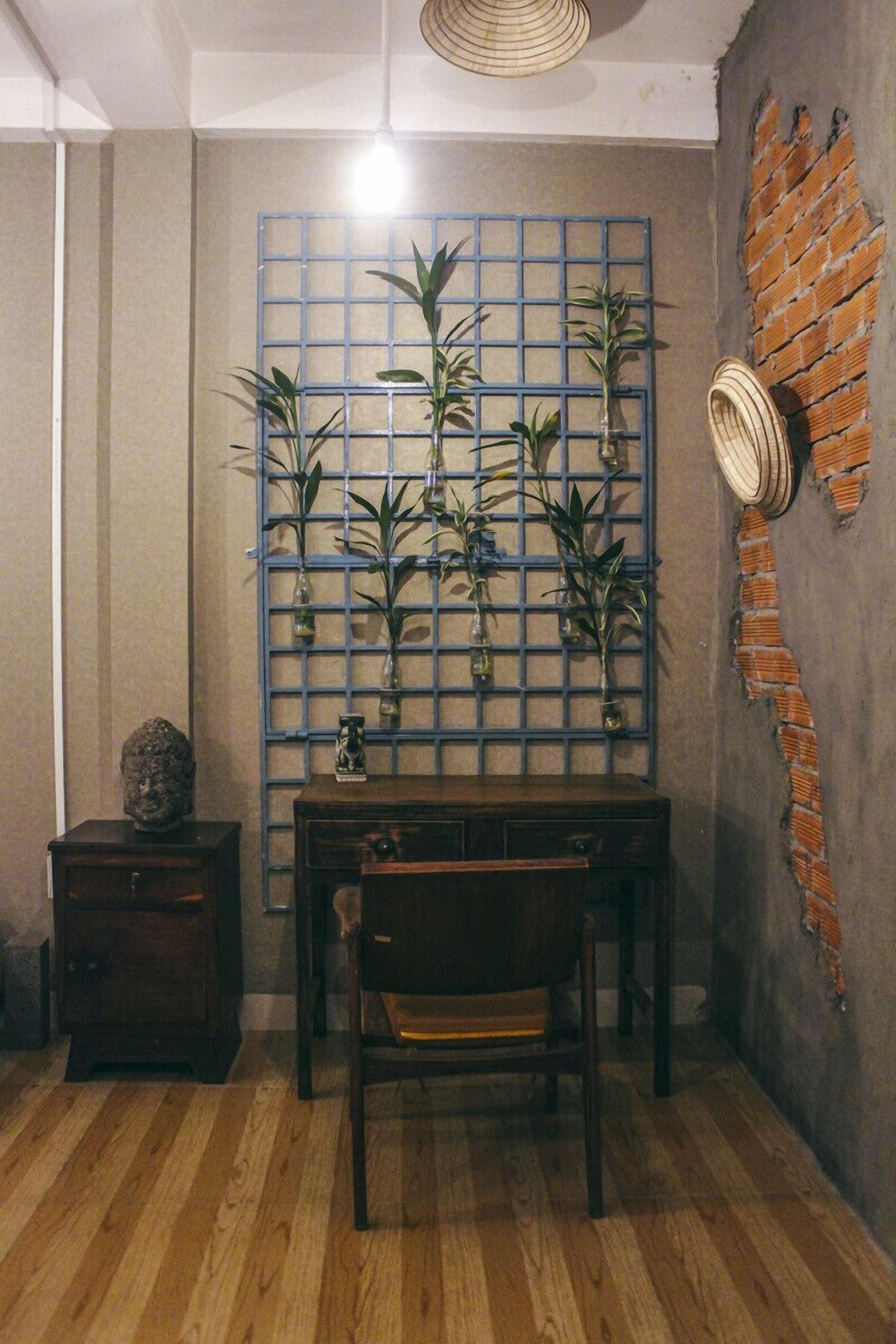 A room with a wooden floor, a table with chairs, a blue grid wall with potted plants, and a brick wall with a woven basket.