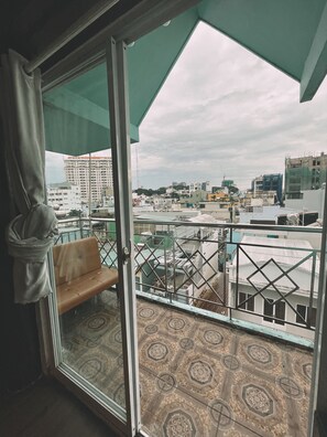A balcony with a patterned floor, a bench, and a view of a cityscape with buildings and a cloudy sky. - Nha Saigon (Ho Chi Minh City)