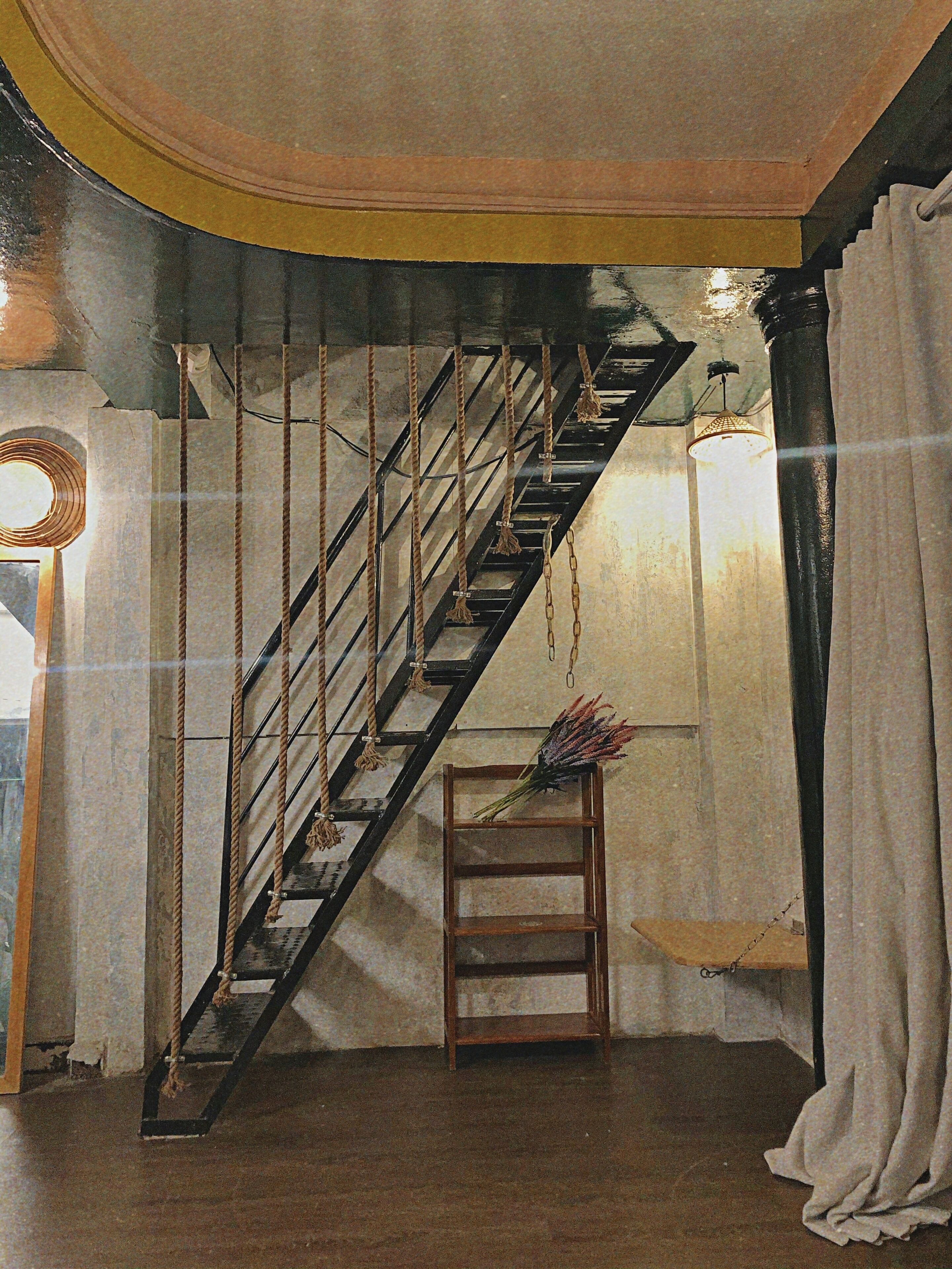 Una escalera con barandilla de madera y un taburete de madera con un ramo de flores.