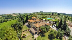 A large villa with a swimming pool, surrounded by lush greenery and vineyards.