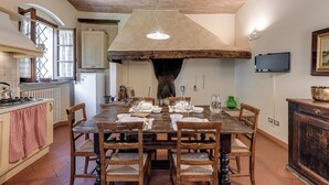 A rustic kitchen with a large wooden table set for dining, a chimney, and a television on the wall.