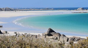Un paysage côtier caractérisé par une plage de sable, des eaux turquoise et limpides, et des affleurements rocheux.