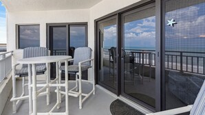 A balcony with white furniture, including a table and chairs, and a glass door leading to a view of the ocean. - Luxury 2/2 Condo with the Best Ocean View! (New Smyrna Beach)