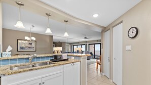 A kitchen with granite countertops, white cabinets, a double sink, pendant lighting, and a ceiling fan. - Luxury 2/2 Condo with the Best Ocean View! (New Smyrna Beach)