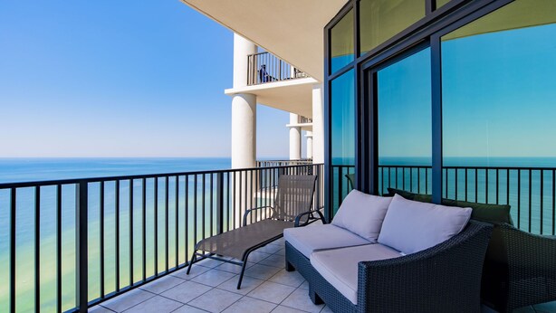 A balcony with a view of the sea, a wicker sofa, and a chair.