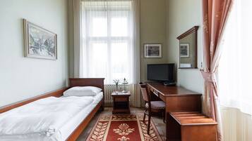 Ein Hotelzimmer mit Bett, Schreibtisch, Stuhl, Fernseher und einem Fenster mit Vorhängen.
