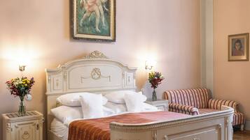 A bedroom with a large bed, two bedside tables, a nightstand, a sofa, and a painting on the wall.