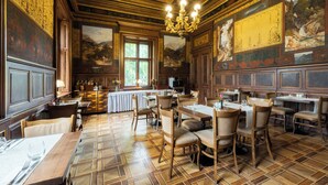 A dining area with wooden tables and chairs, a chandelier, and a large mural on the wall. - Vila Lanna (Prague)