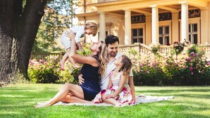 A family sitting on a blanket in a park with a building in the background. - Vila Lanna (Prague)