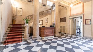 A lobby with a checkered floor, a staircase, a reception desk, and columns. - Vila Lanna (Prague)