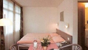 A hotel room with a bed, a table with a vase of flowers, a lamp, and a chair. - Hotel Post Vista (Zweisimmen)