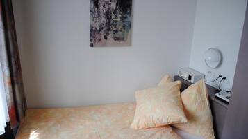 Una cama individual con una colcha estampada y dos almohadas, una mesita de noche con una lámpara, y un cuadro colgado en la pared.
