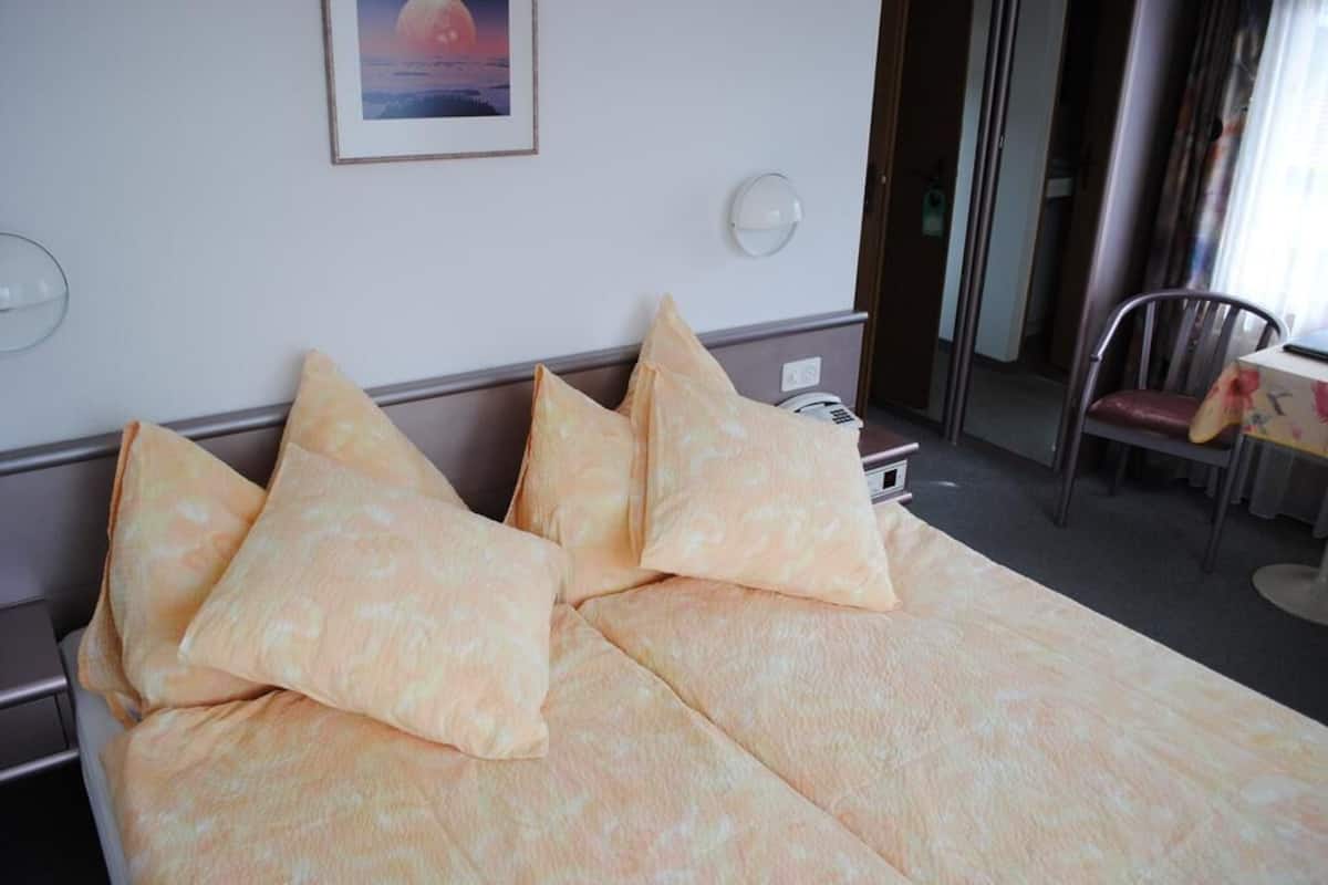 A hotel room with a bed, pillows, a bedside table, a lamp, a chair, and a framed picture on the wall.
