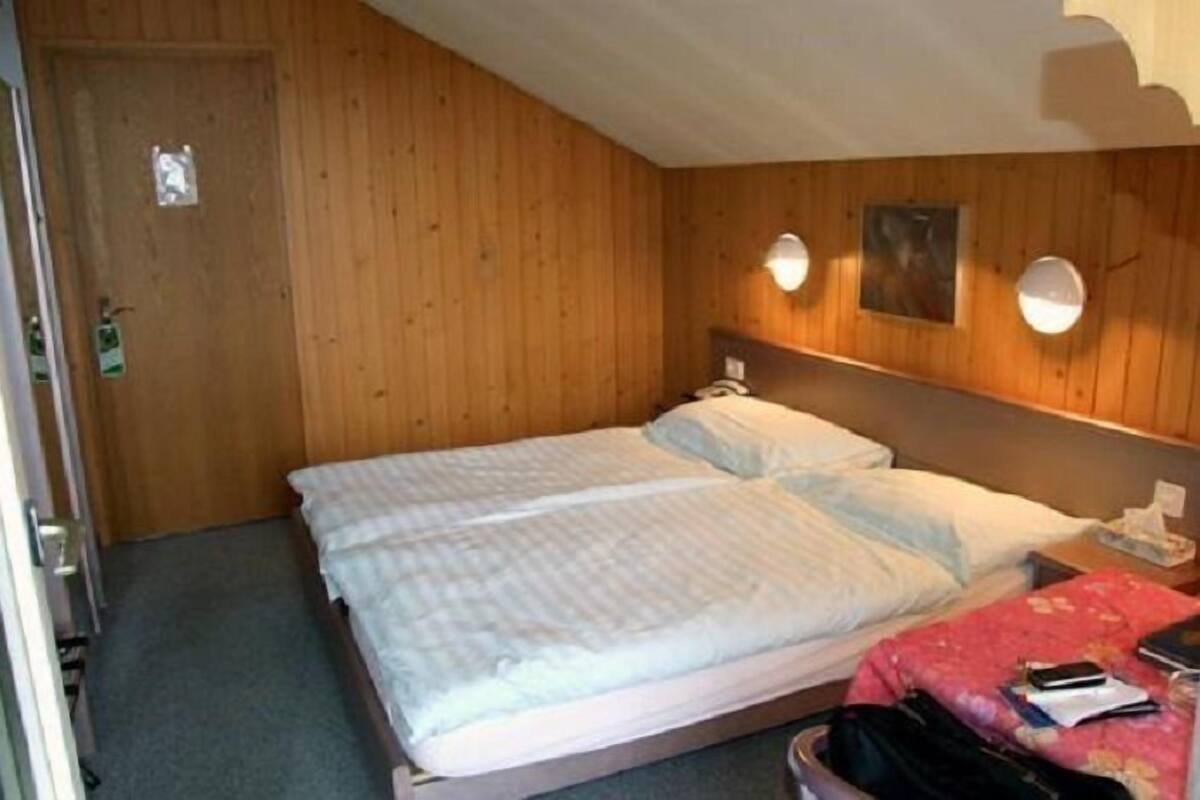 A single bed with a wooden headboard, a bedside table with a lamp, and a small wall-mounted picture.