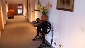 A hallway with a bed at the end, a vase with flowers, and a framed picture on the wall. - Hotel Post Vista (Zweisimmen)