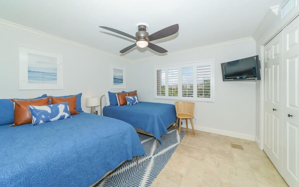 A bedroom with two beds, a ceiling fan, a TV, and a window with blinds.