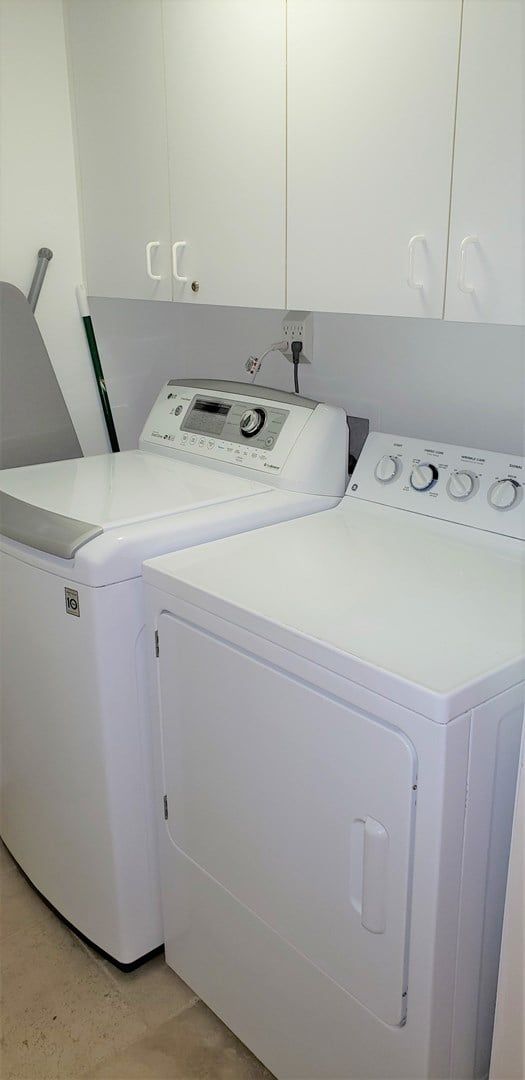 A laundry area with two white washing machines and a dryer, a cabinet above, and a power outlet on the wall.