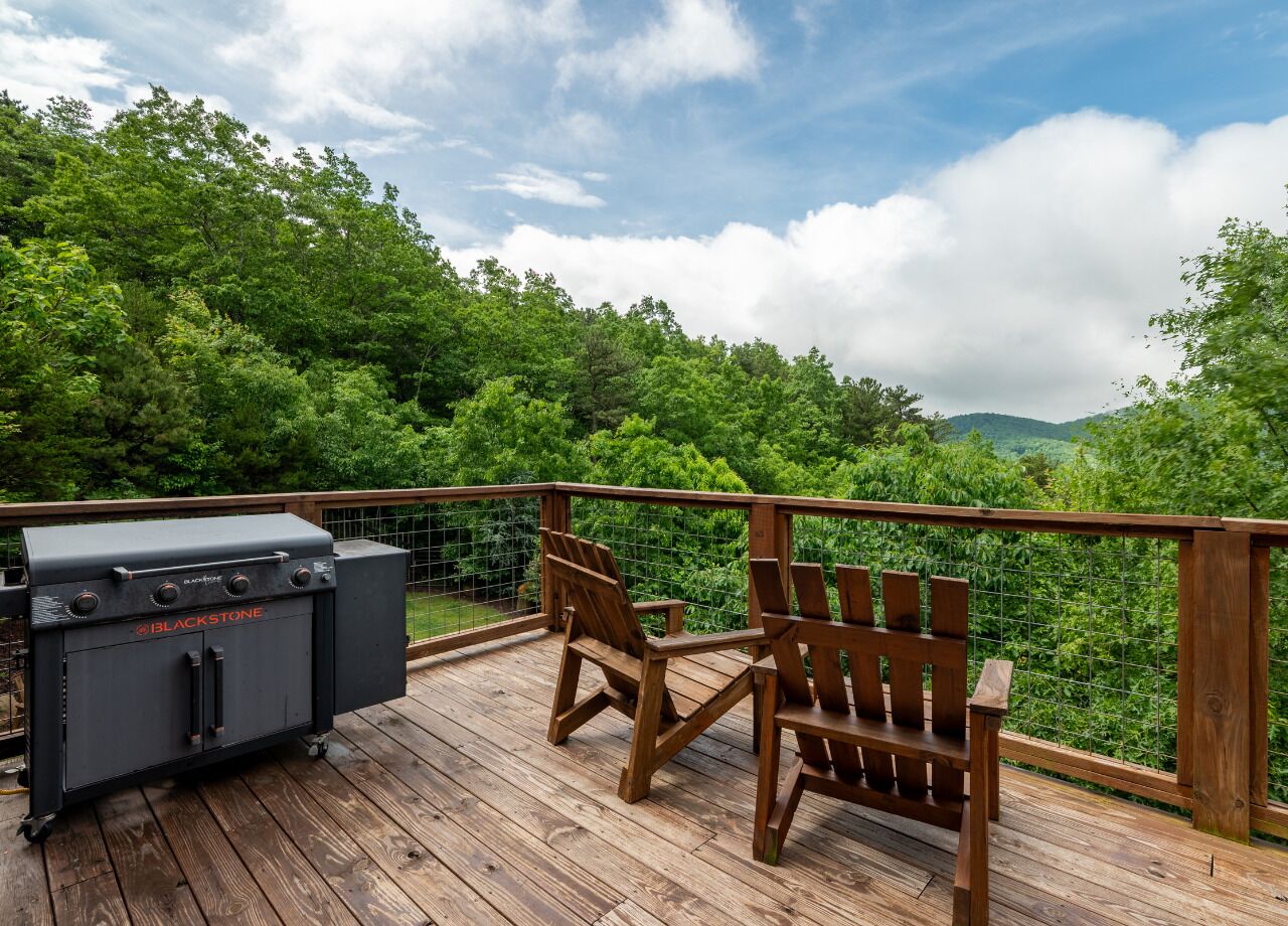 A wooden deck with a grill and chairs overlooking a lush green landscape.