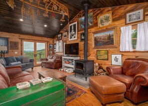 A cozy cabin interior with a fireplace, leather furniture, and framed pictures on the walls. - The Brindle Barn | Pet Friendly, Fenced Yard & Stunning Views (Black Mountain)