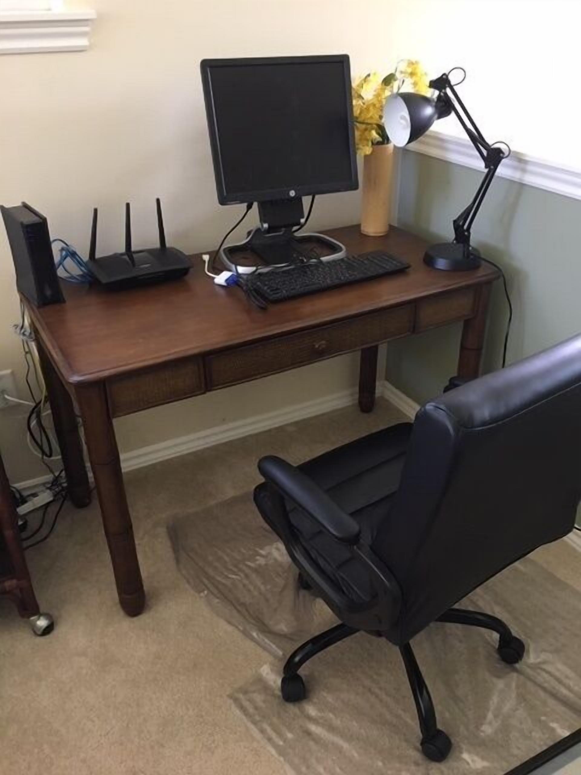 Ein Holztisch mit einem Computerarbeitsplatz, inklusive Bildschirm, Tastatur und Lampe.
